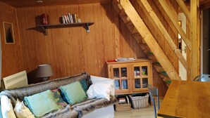 A cozy room with a wooden ceiling, a sofa with patterned cushions, a table, and a cabinet with glass doors.