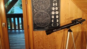 A wooden-paneled room with a poster of the night sky, a telescope on a tripod, and a door leading outside.