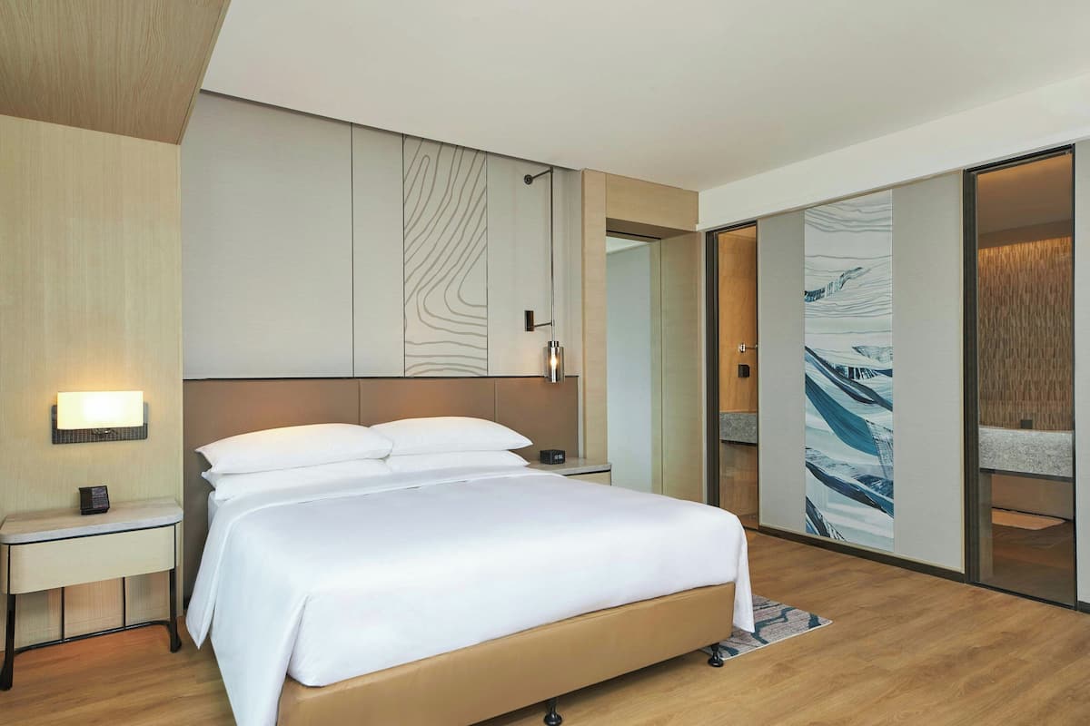 Ein modernes Hotelzimmer mit einem großen Bett, einem Nachttisch, einer Wandleuchte und einer Schiebetür zu einem Badezimmer.