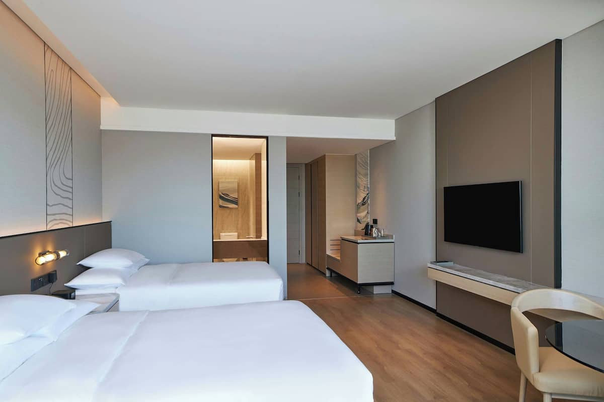 Ein modernes Hotelzimmer mit zwei Betten, einem Fernseher, einem Schreibtisch und einem Badezimmer.