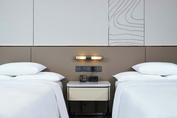 A hotel room with two beds, a bedside table with a phone and clock, and a wall-mounted light fixture. - Courtyard by Marriott Changchun (Changchun)
