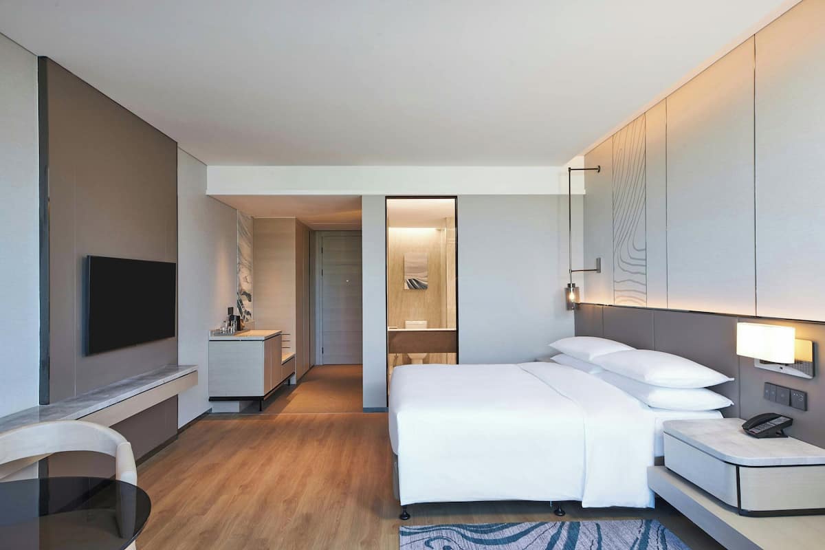 Ein modernes Hotelzimmer mit einem großen Bett, einem Nachttisch und einem wandmontierten Flachbildfernseher.