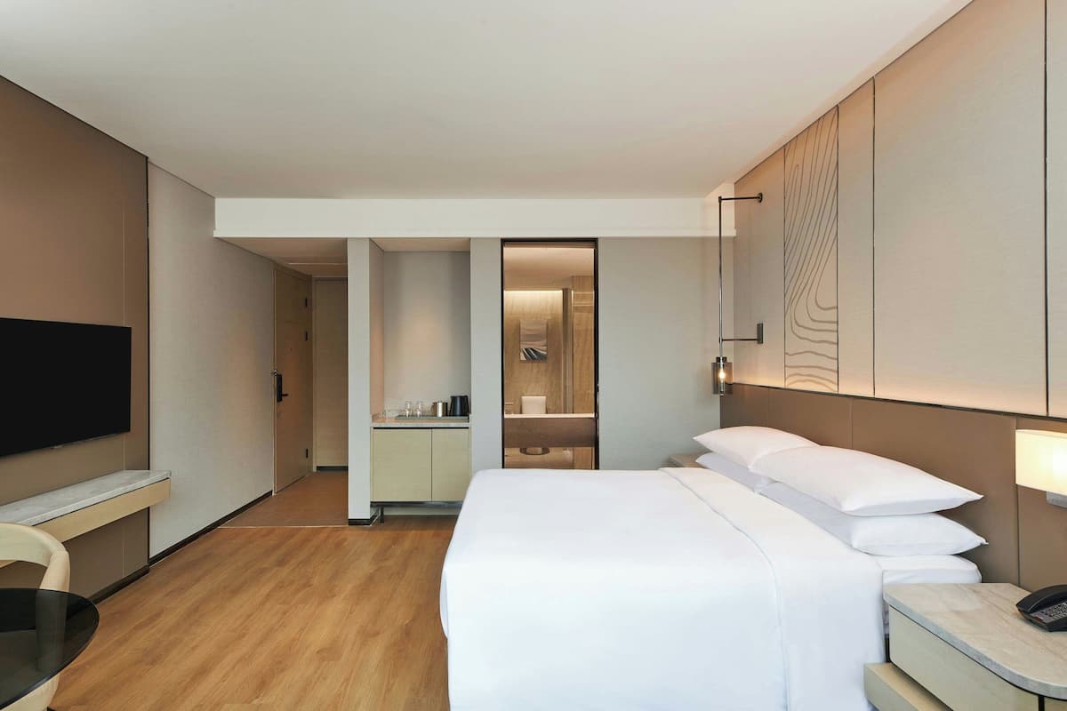 Ein modernes Hotelzimmer mit einem großen Bett, einem Schreibtisch, einem Flachbildfernseher und einem separaten Badezimmer.