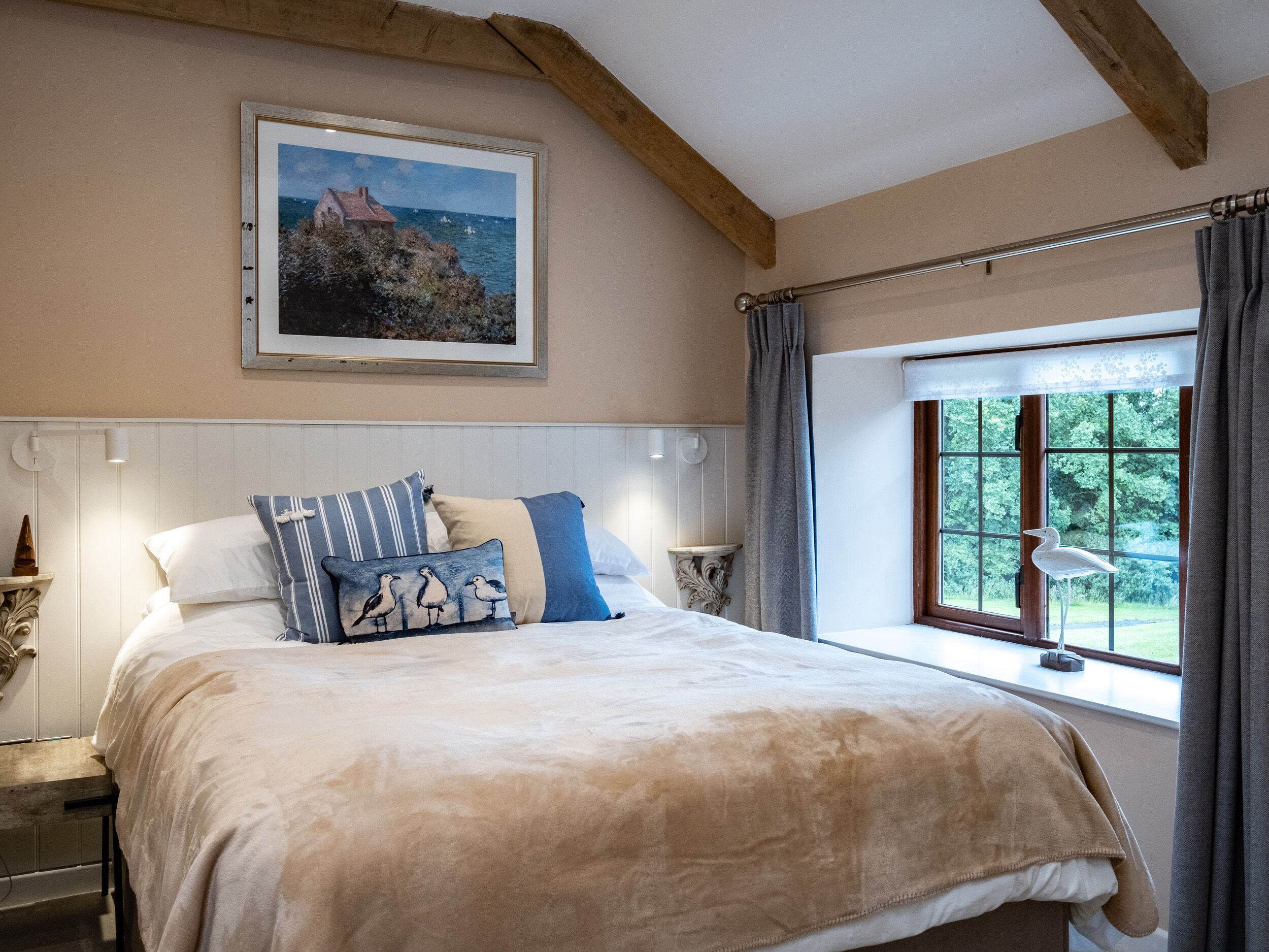 Un dormitorio con una cama grande, un cuadro en la pared, una ventana con cortinas y una viga de techo de madera.
