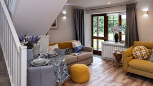 Una sala de estar acogedora con una escalera, un comedor con una mesa dispuesta para dos personas y vistas a través de un ventanal.