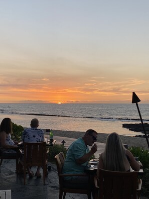 A sunset view from a seaside restaurant with outdoor seating.