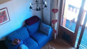 A cozy living room with a blue sofa, a wooden dining table, and a chandelier. - 100m from resort center, 1st floor, balcony, parking, tv, ski locker, 20m², Valloire (Valloire)