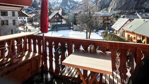 A wooden balcony with a table and chairs, overlooking a snow-covered village and mountains. - 100m from resort center, 1st floor, balcony, parking, tv, ski locker, 20m², Valloire (Valloire)