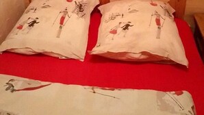 A wooden cabin-style room with a bed featuring a red bedspread and two pillows with a ski-themed design. - 100m from resort center, 1st floor, balcony, parking, tv, ski locker, 20m², Valloire (Valloire)