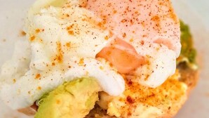 Un plato de desayuno con un huevo pochado, aguacate y condimentos.