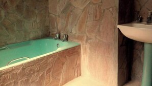 Un baño con pared de piedra, una bañera y un lavabo.