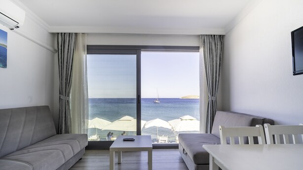 Quarto moderno com sofá, uma pequena mesa e vista para o mar através de uma grande janela.