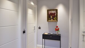 Um corredor com portas brancas, um aparador preto com um vaso de flores vermelhas e uma obra de arte emoldurada na parede.
