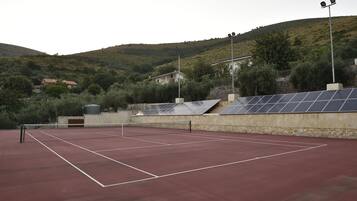 A tennis court with a net, surrounded by stone walls and solar panels.