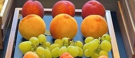 A wooden fruit tray with peaches, grapes, and an orange on a table.