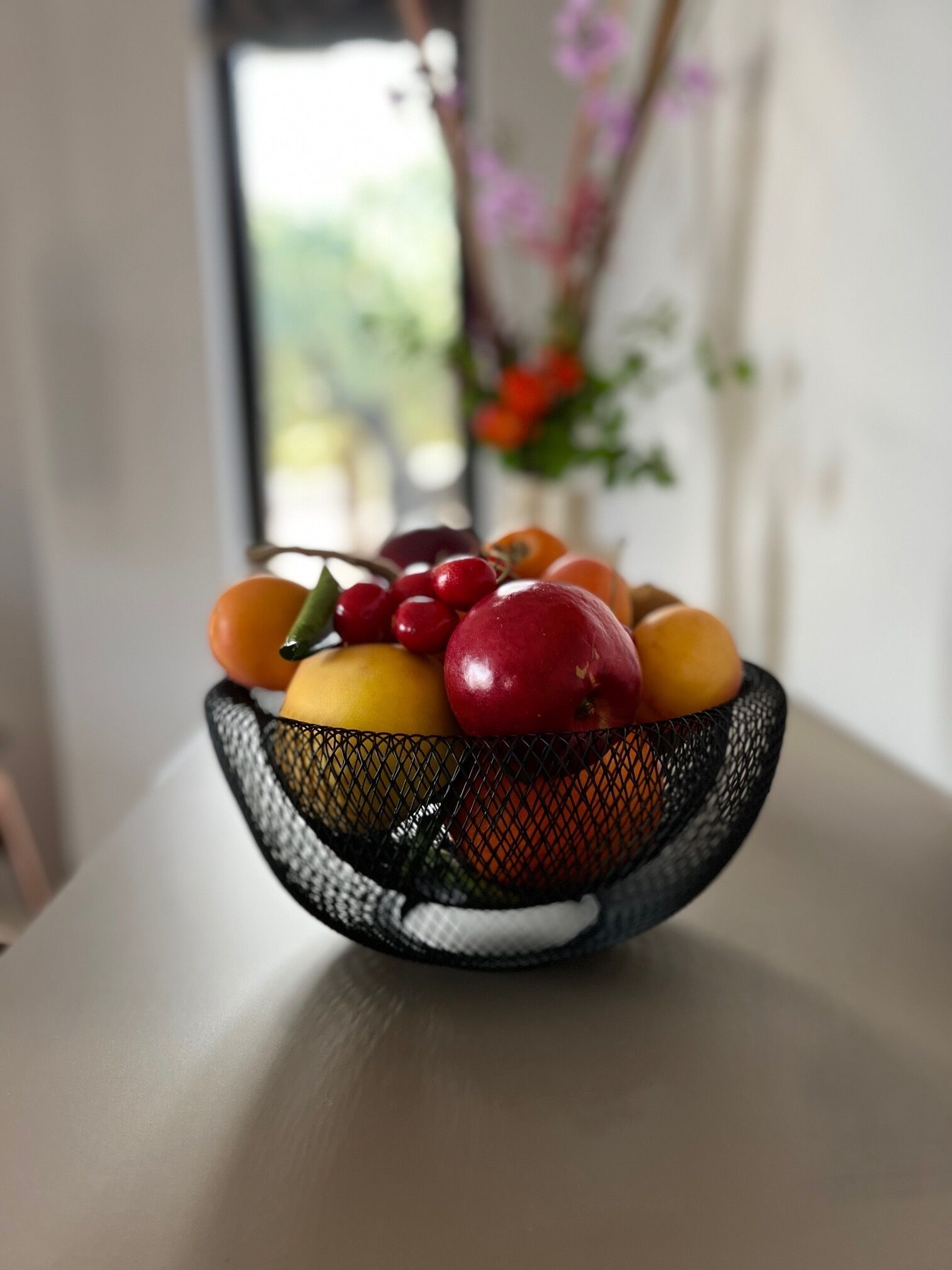 A black wire basket containing various fruits on a table.