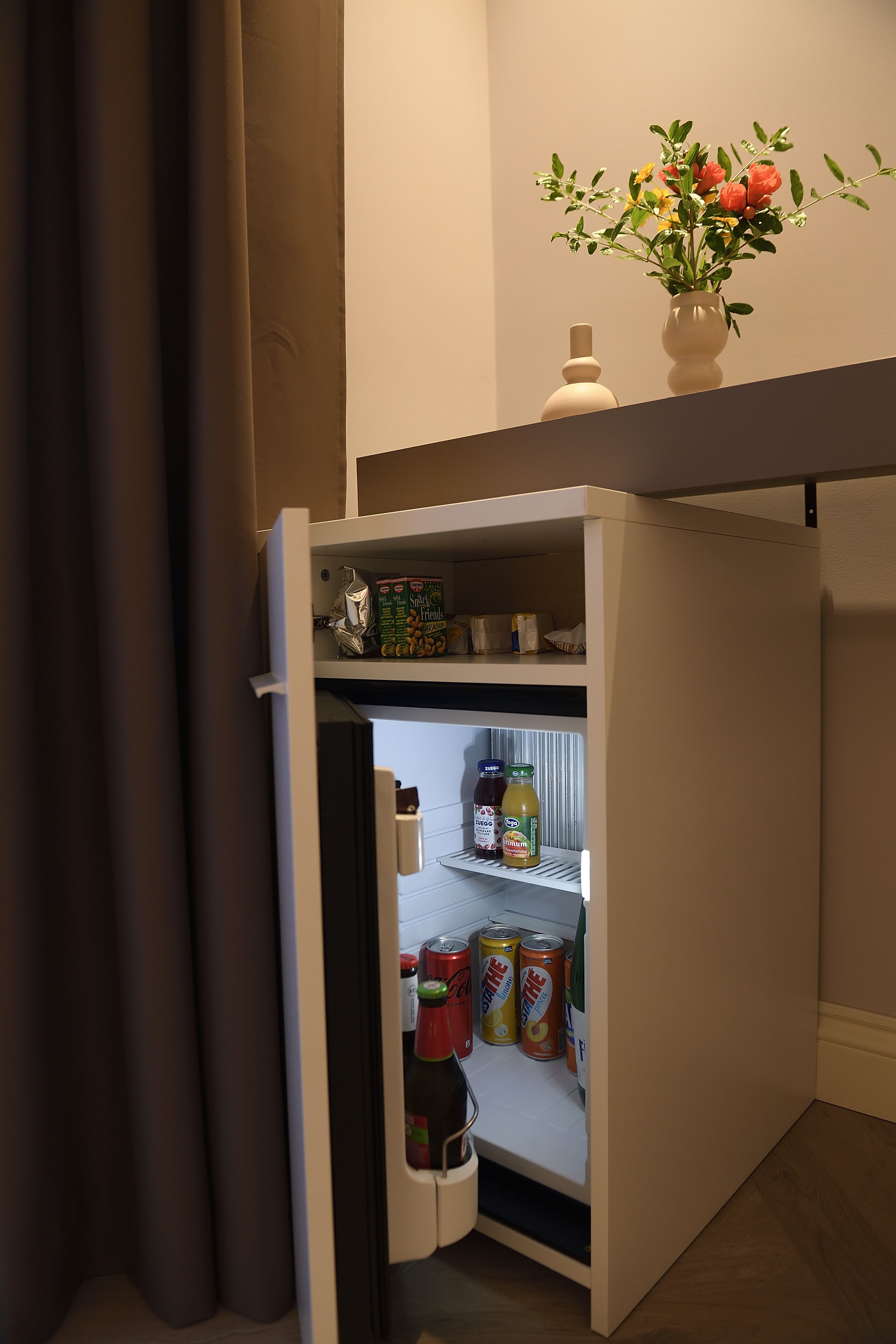A compact refrigerator with a small freezer compartment, containing various food items and beverages.