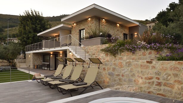 Uma casa moderna com fachada de pedra, varanda com espreguiçadeiras e uma banheira de hidromassagem.