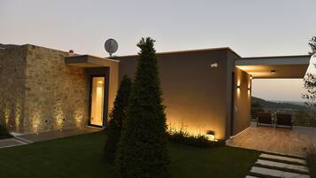 A modern house with a stone facade, a satellite dish, and a well-lit patio with outdoor seating.