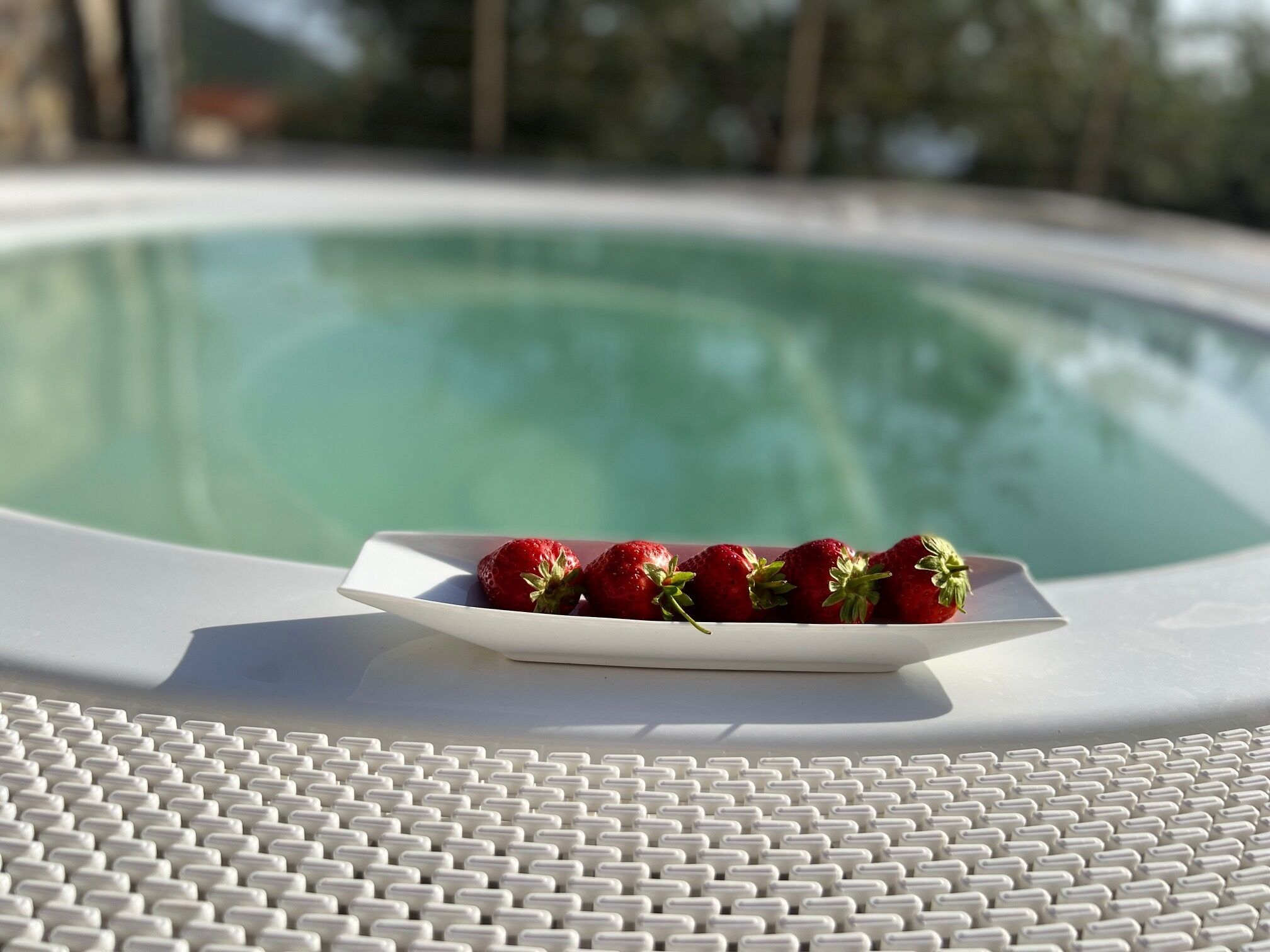 A white poolside table with a white tray holding strawberries.