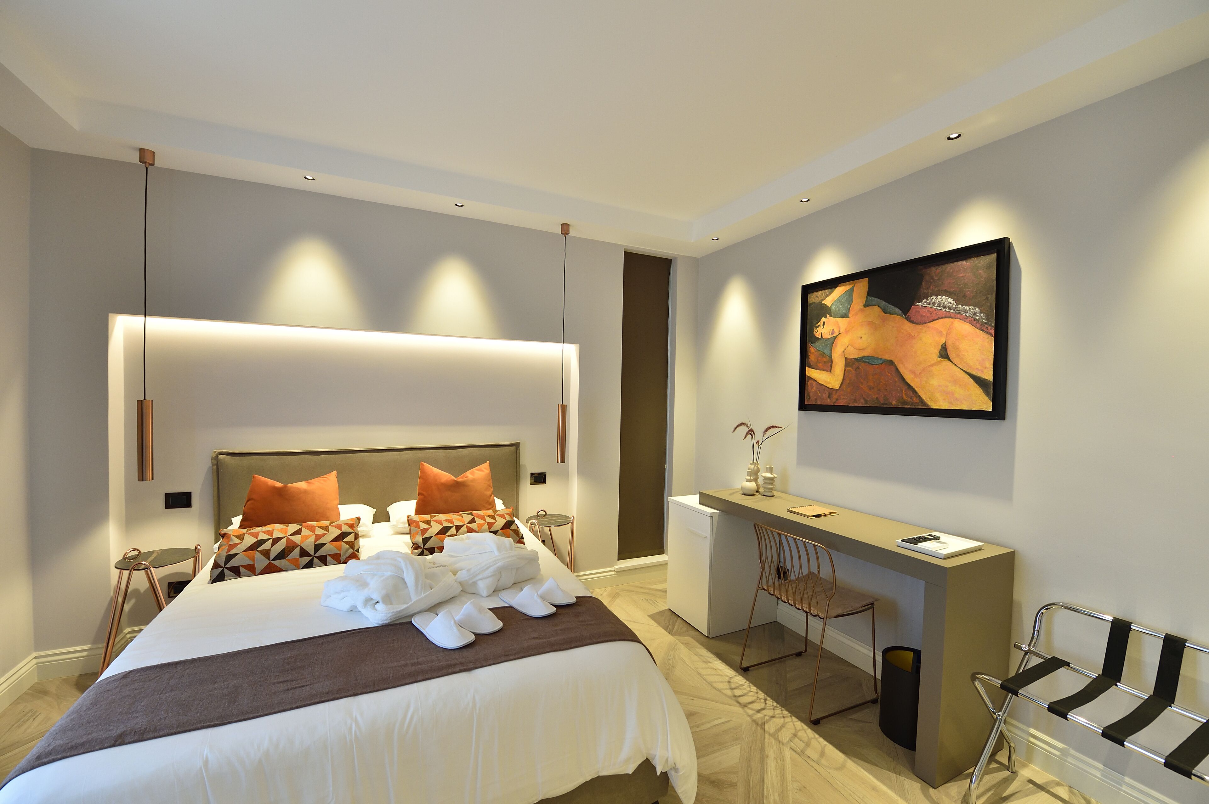 A modern hotel room with a large bed, a desk, and a painting on the wall.
