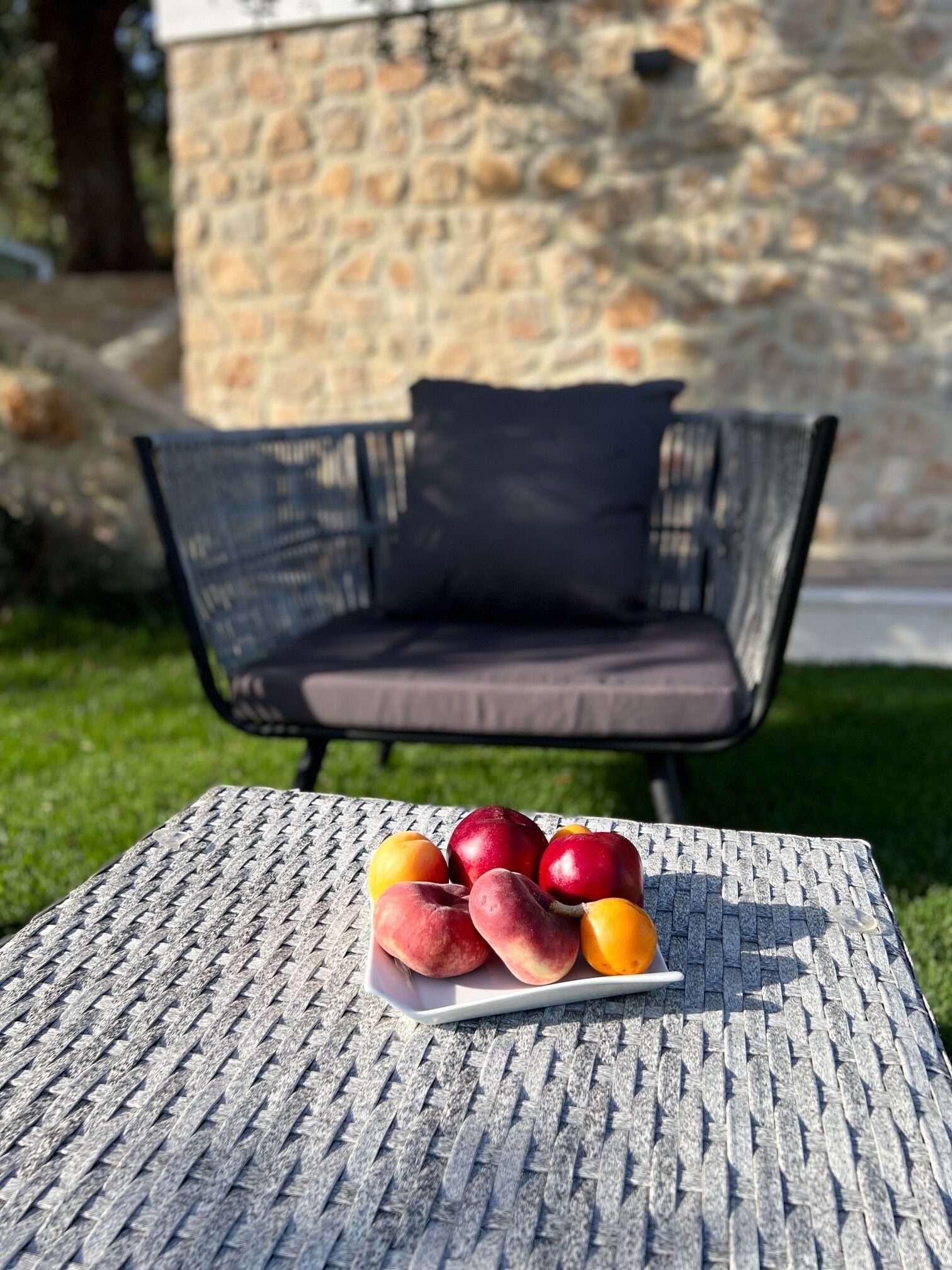 Une table en osier avec une assiette de fruits, le tout installé à l’extérieur.