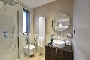 Une salle de bain moderne avec une douche à parois de verre, des toilettes, un lavabo avec un miroir rond et un meuble-lavabo avec un porte-serviettes.