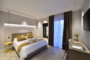 A modern hotel room with a large bed, a desk with a chair, a flat-screen TV, and a vase with flowers.