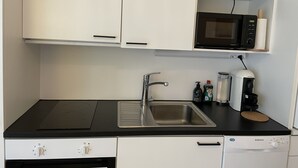 Una cocina compacta con armarios blancos, encimera negra, pileta de acero inoxidable, microondas, cafetera y lavavajillas.