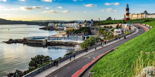 A coastal town with a prominent lighthouse, a curved road, and a waterfront promenade.