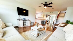 A living room with a sofa, coffee table, and TV. There is a staircase leading to another level. - Spacious Beach Farmhouse w/ Backyard Oasis (Vero Beach)