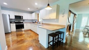 A kitchen with white cabinets, stainless steel appliances, and a wooden floor. - Spacious Beach Farmhouse w/ Backyard Oasis (Vero Beach)