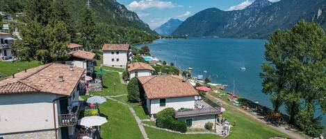 A lakeside village with terraced houses, a swimming pool, and a view of the lake and mountains.