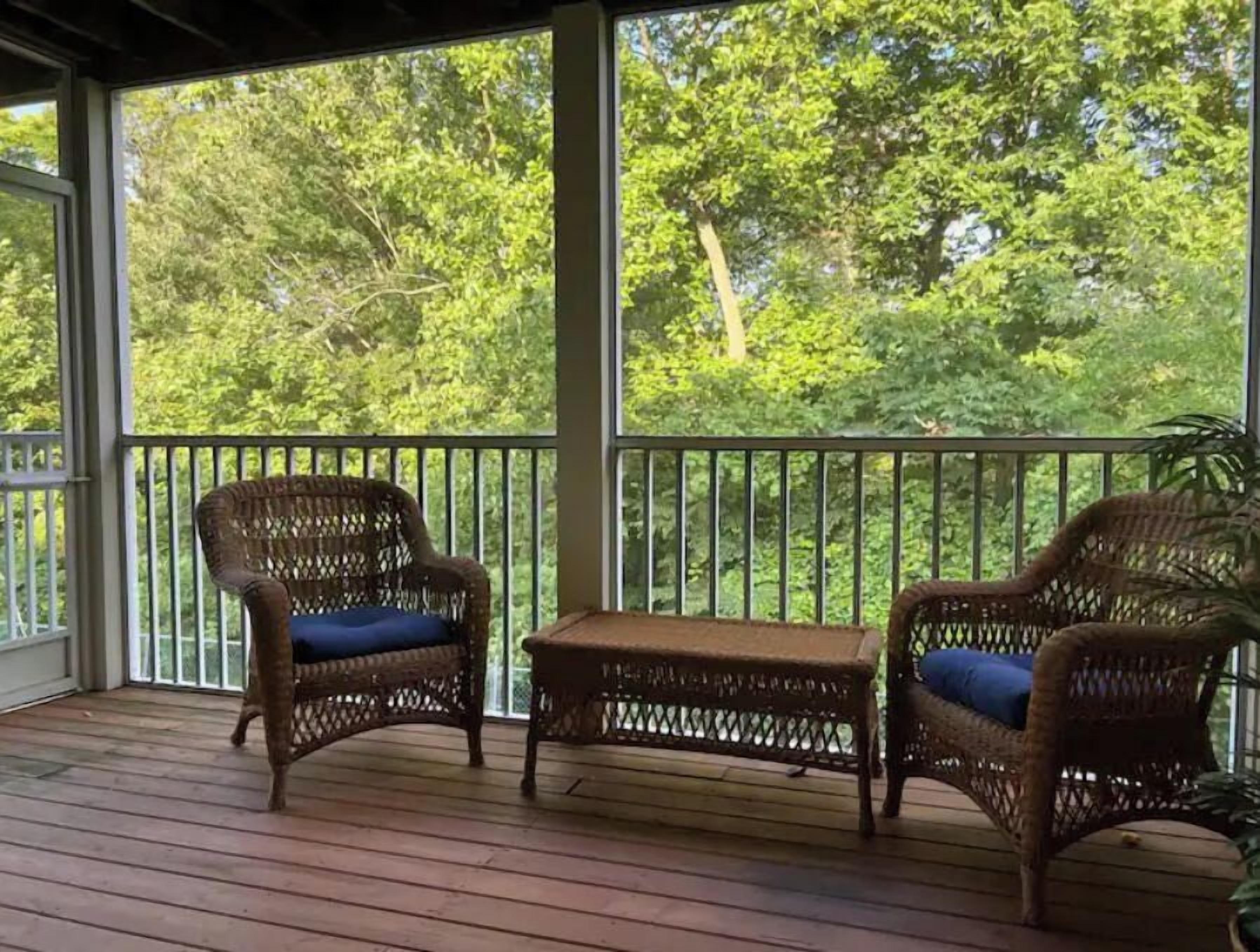 A covered porch with wicker furniture and a view of a forest.