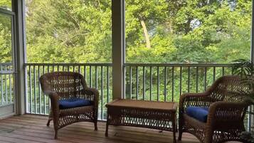 A covered porch with wicker furniture and a view of a forest.