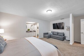 A modern bedroom with a bed, a gray sofa, and a TV.