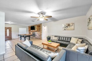 A spacious living room with a dark leather sofa, a wooden coffee table, and a pool table.