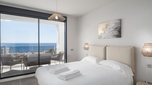 Et soveværelse med en stor seng, havudsigt og en balkon med stole.