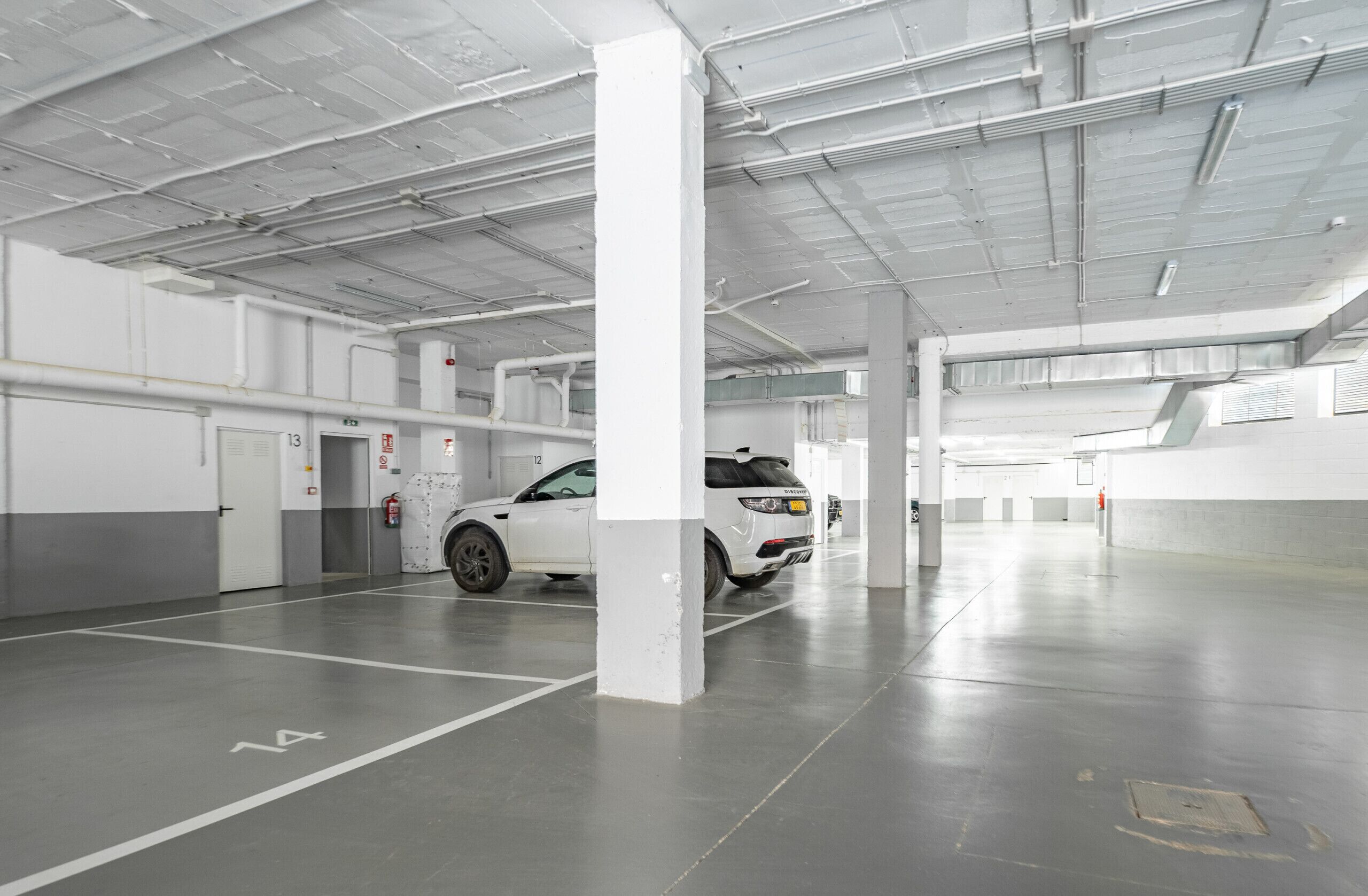 A spacious indoor parking area with white pillars and a white car parked in a designated space.