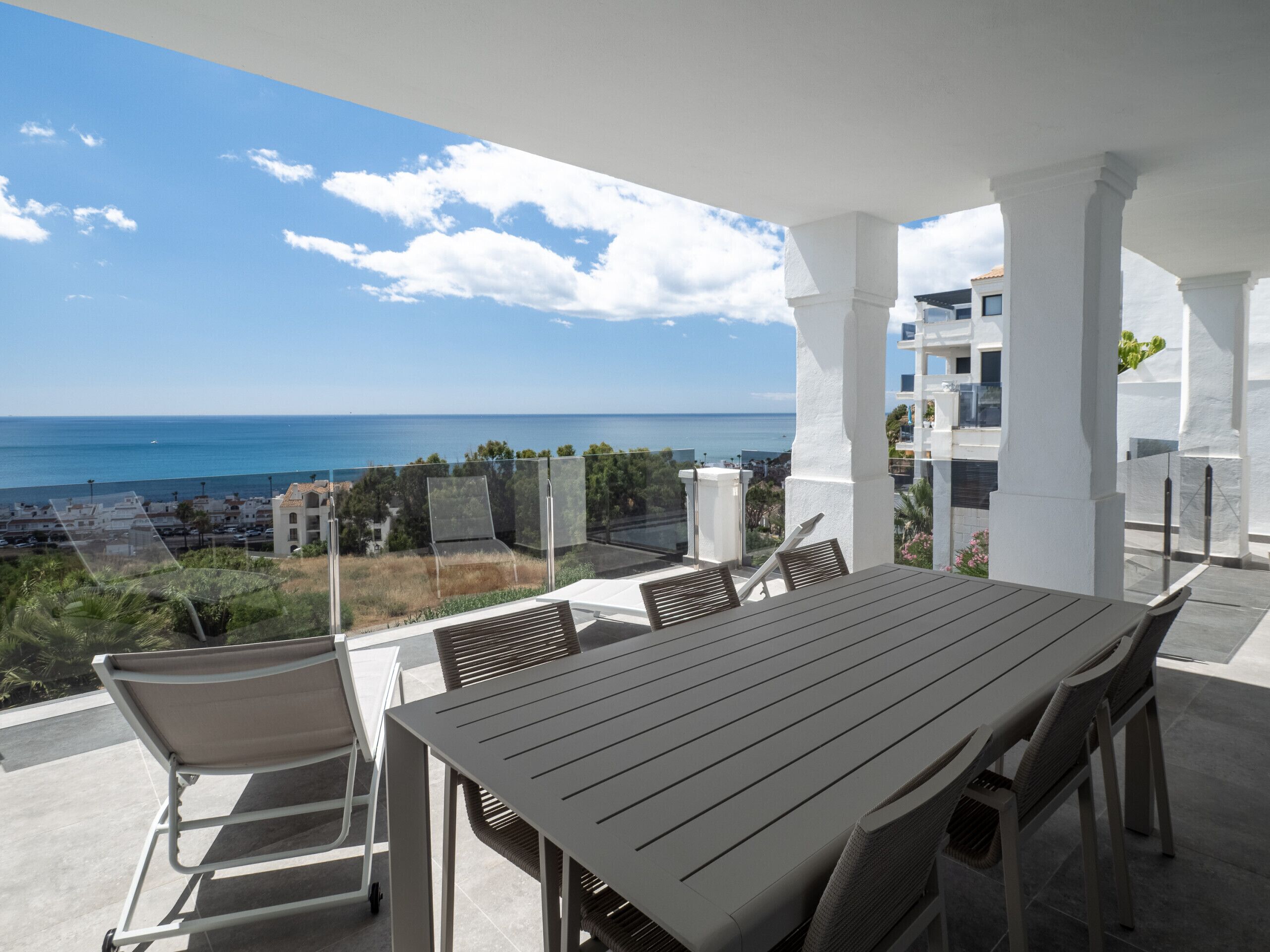 An outdoor patio with a table and chairs, overlooking a coastal view with buildings and greenery.
