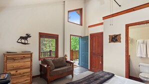 A bedroom with a bed, a dresser, a sofa, a window, and a door leading to a balcony. - Queen - Queen bedroom with private bathroom, mini fridge (Olney)