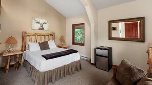 A bedroom with a large bed, wooden headboard, a nightstand with a lamp, a dresser, and a mirror on the wall. - Queen - Queen bedroom with private bathroom, mini fridge (Olney)