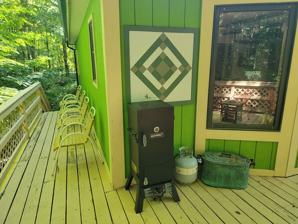 Een groen gebouw met een gasfles en een metalen kast met de aanduiding 'Masterbuilt' op de veranda.