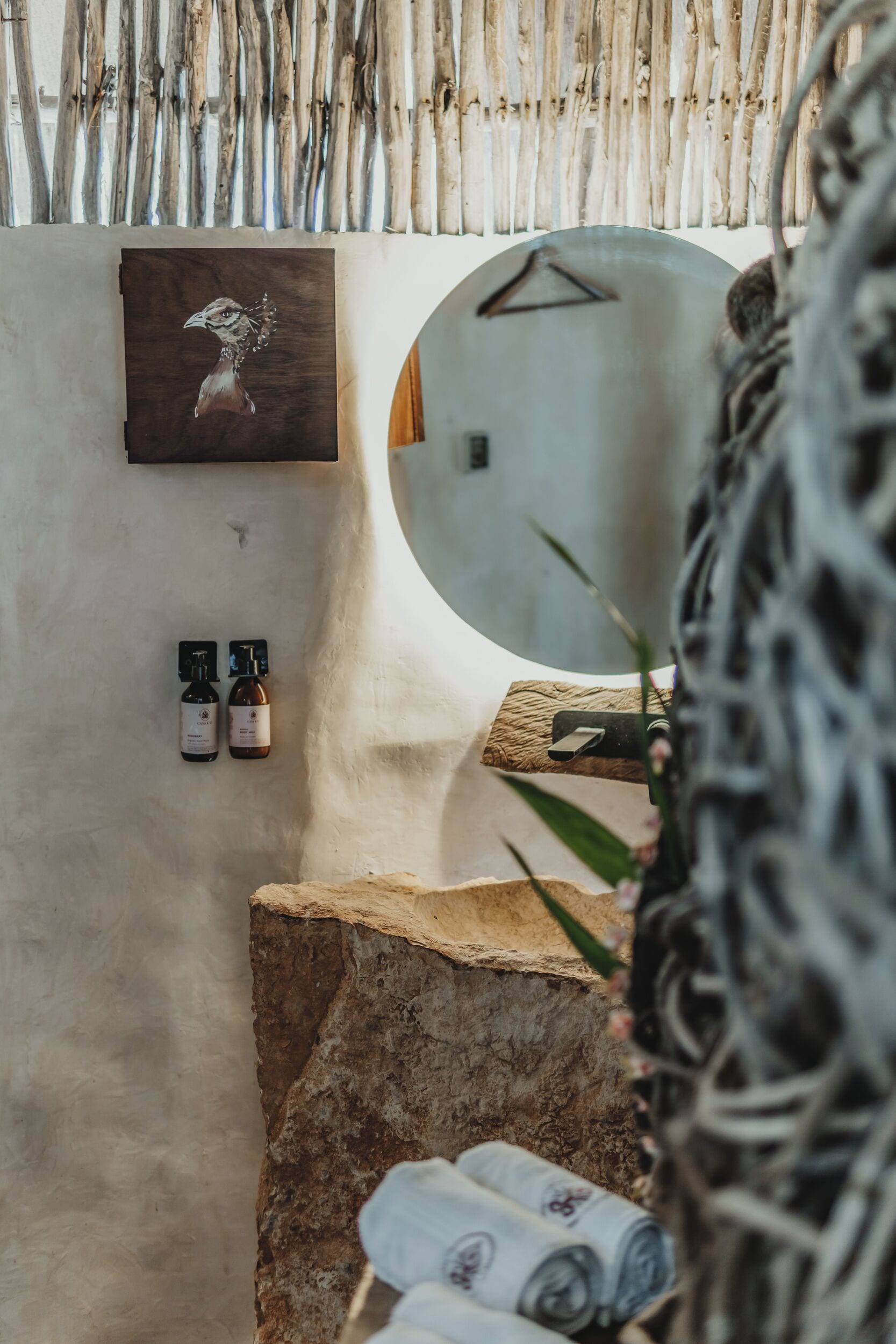 A spa area with a wooden wall, a round mirror, two bottles of essential oils, and a stone bench.