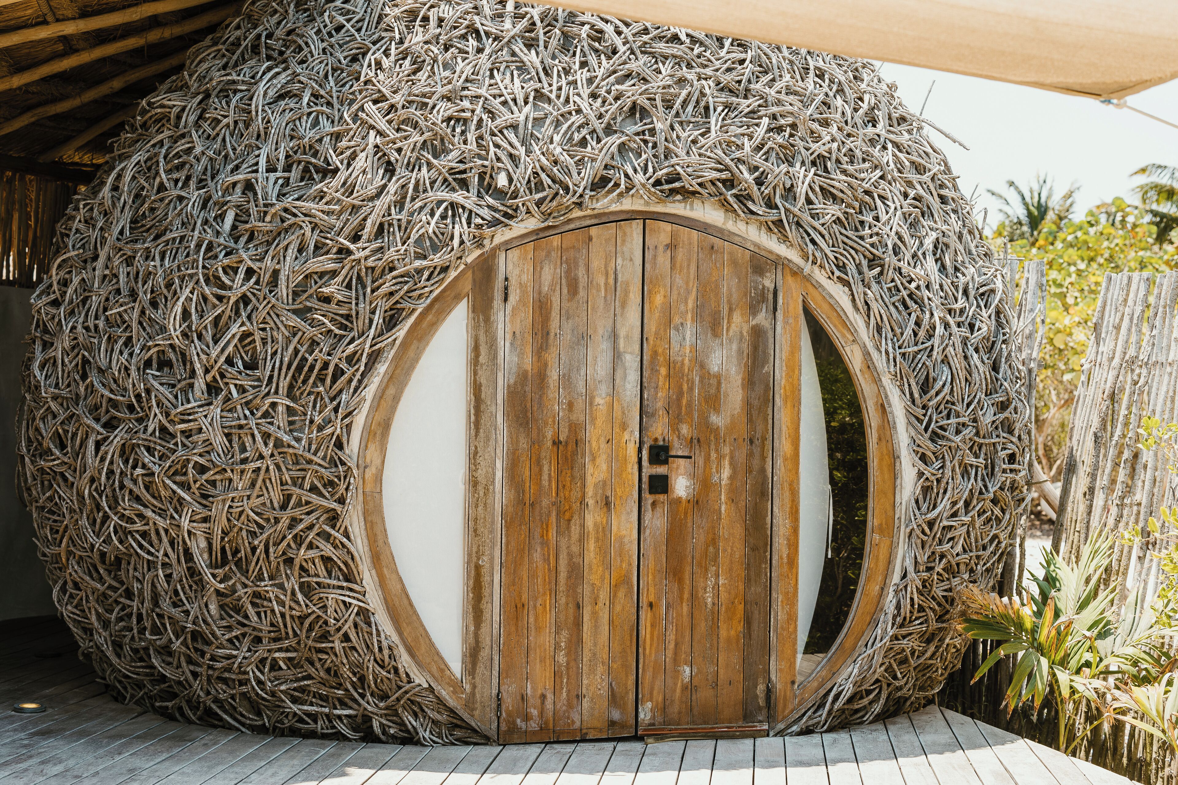 A round, straw-wrapped structure with a wooden door, suggesting a rustic, eco-friendly design.