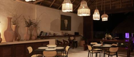 An outdoor dining area with wicker chairs and tables, hanging wicker chandeliers, and a thatched roof structure.