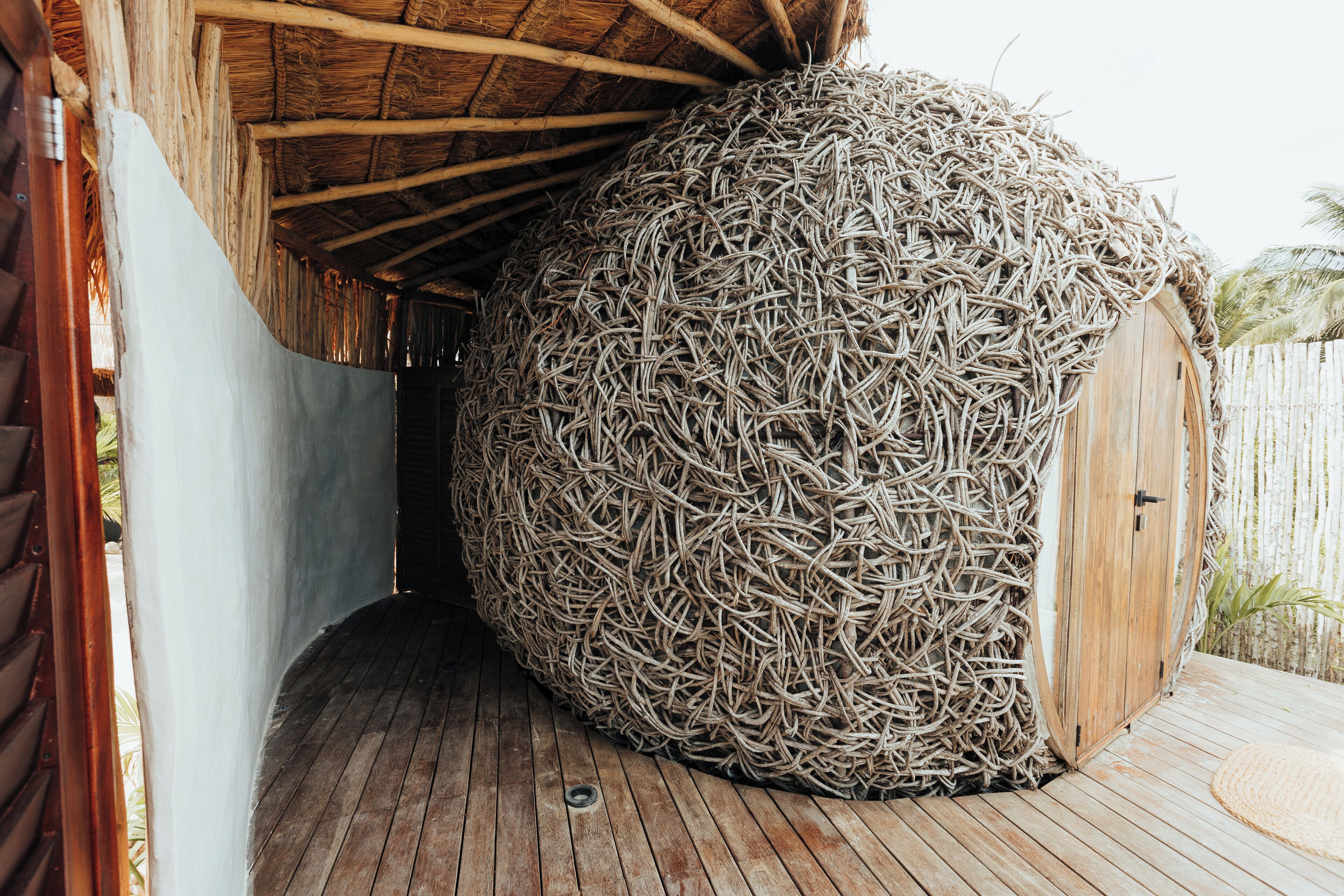 Een rieten gebouw met een houten deur en een houten terras.