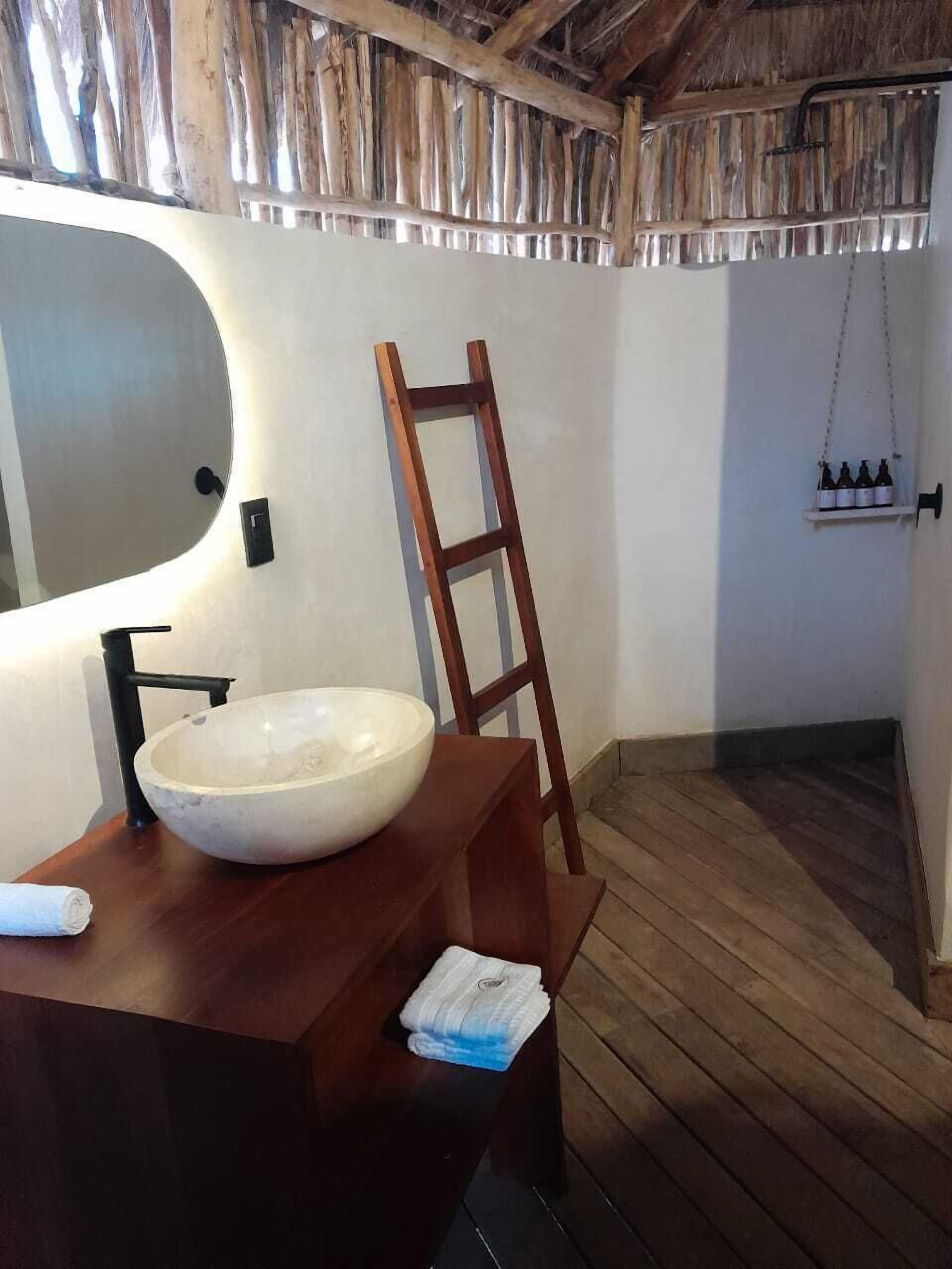 A bathroom with a wooden vanity, a large oval sink, a wooden ladder, and a shelf with bottles.