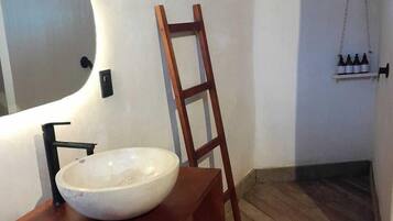 A bathroom with a wooden vanity, a large oval sink, a wooden ladder, and a shelf with bottles.