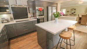Une cuisine moderne dotée d’appareils électroménagers en acier inoxydable, d’un îlot central avec des tabourets et d’un coin repas comprenant une chaise en osier et une table.